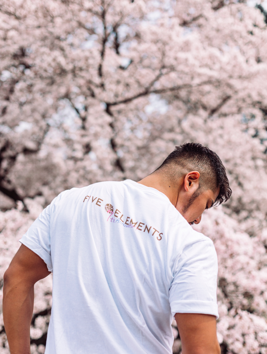 桜の下、鍼灸院ファイブエレメンツ7周年記念Tシャツの筋肉質男性の背中